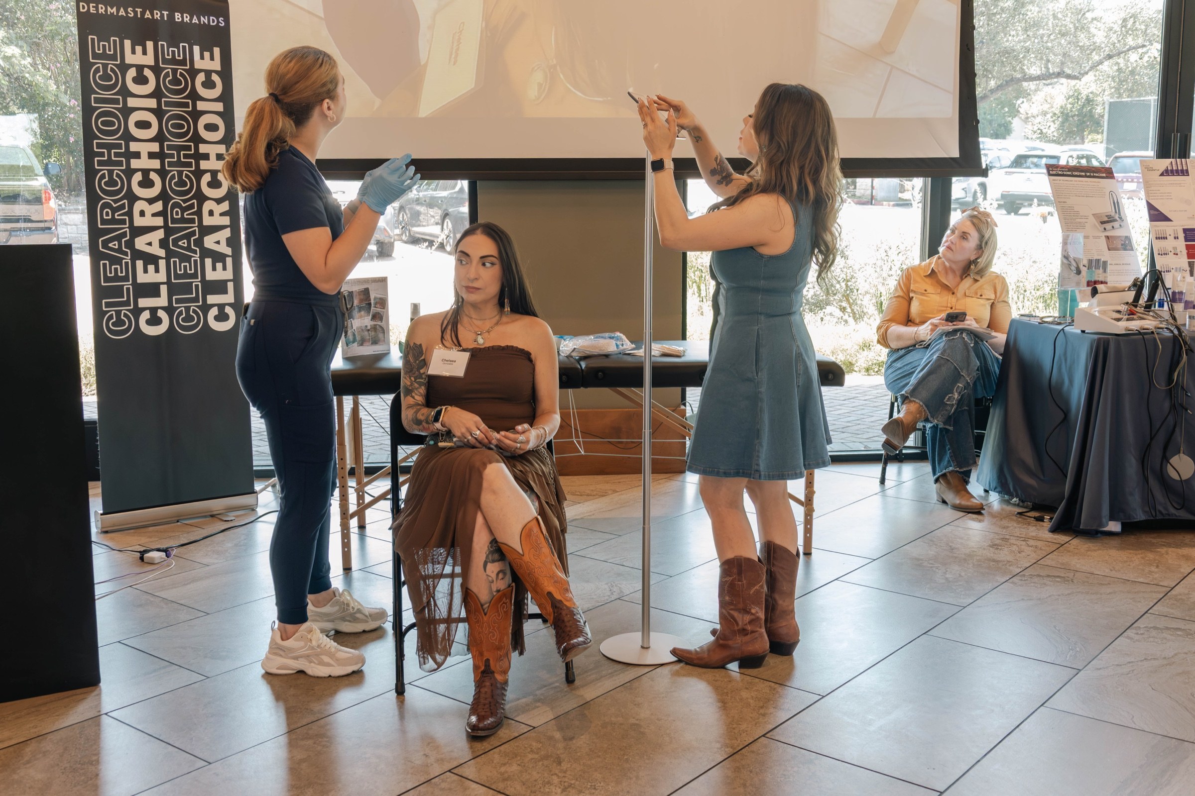 A seated attendee watches a hands-on esthetics demonstration with educators nearby